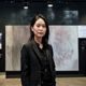 林晓美，资深人体艺术摄影研究者，站立于摄影作品展览墙前，专业气质沉稳